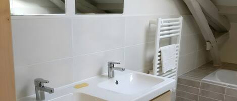 Ein Badezimmer mit einem weißen Waschbecken, zwei Spiegeln, einem Handtuchhalter und einer Badewanne.