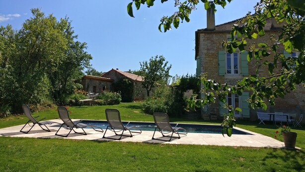 A pool area with lounge chairs, a stone building, and lush greenery.