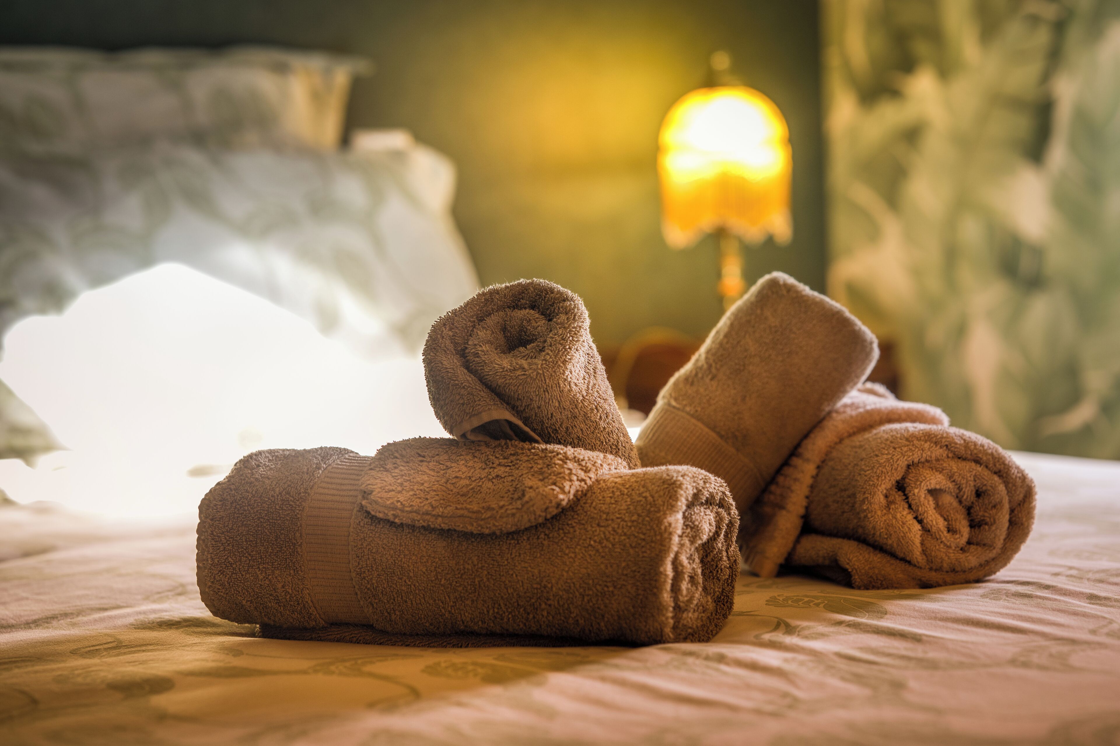 A neatly made bed with rolled towels and a visible headboard.