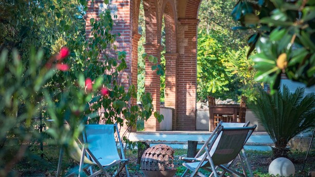 Ein Backsteinbogen über einem Poolbereich mit Liegestühlen und einem Tisch.
