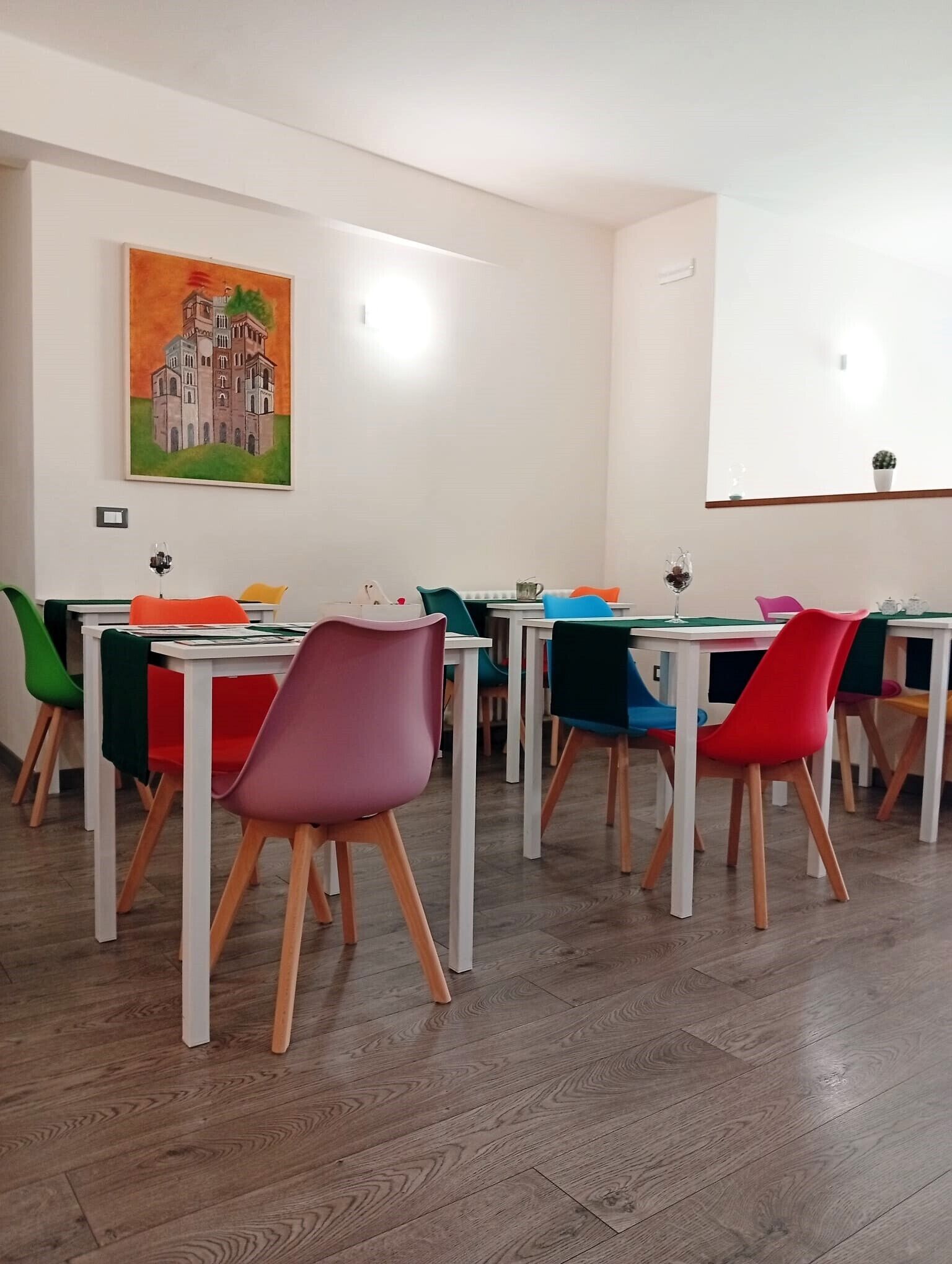 A dining area with multiple tables and chairs, a painting on the wall, and a whiteboard.