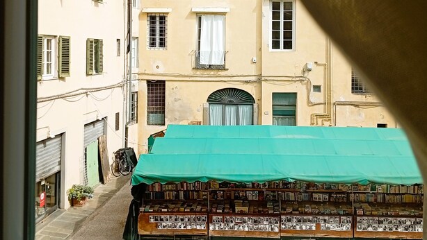 A narrow street with buildings, a green awning, and a window with a view of the street. - Madame Pucci (Lucca)