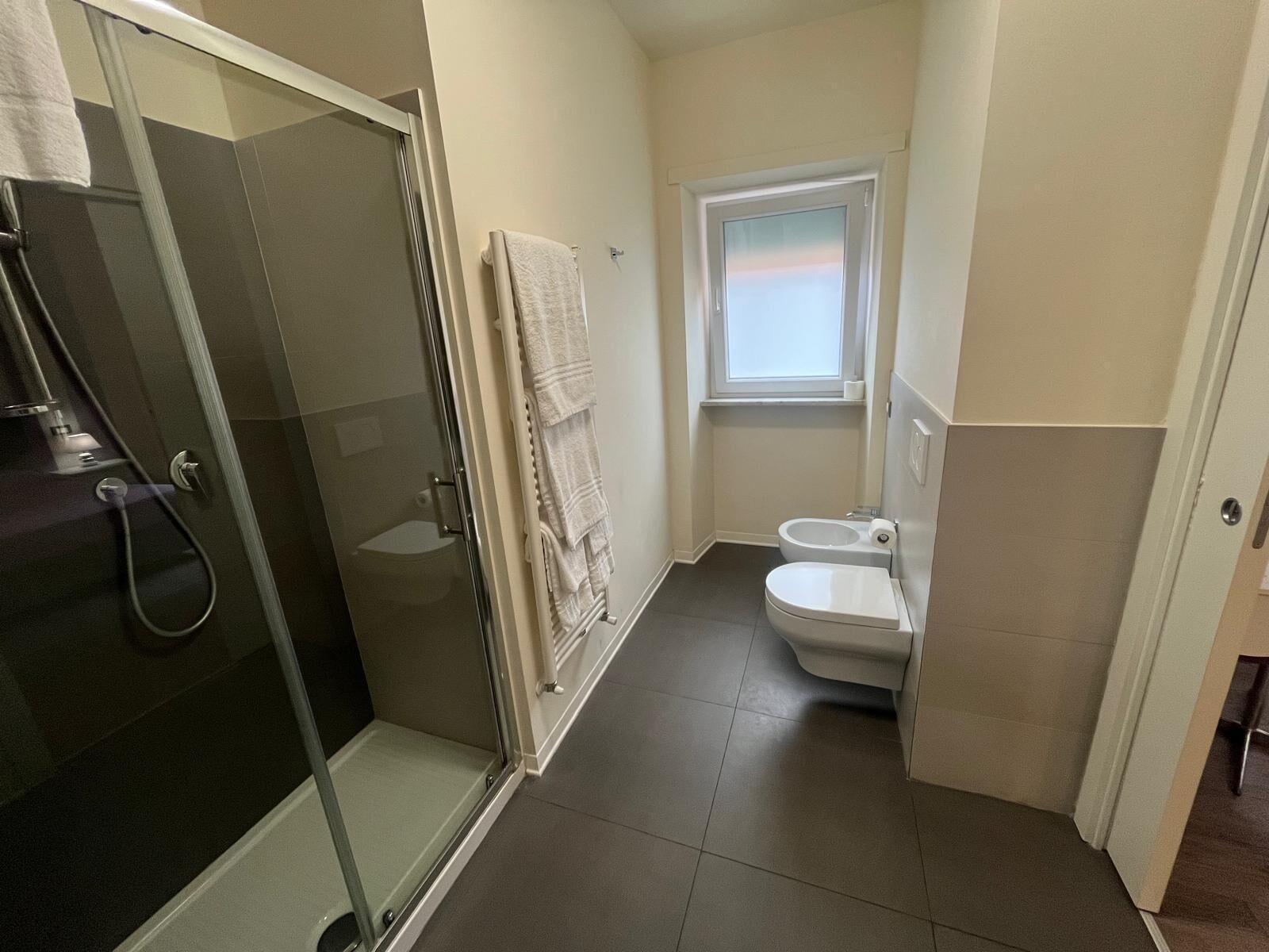 A bathroom with a glass shower enclosure, a toilet, and a window.