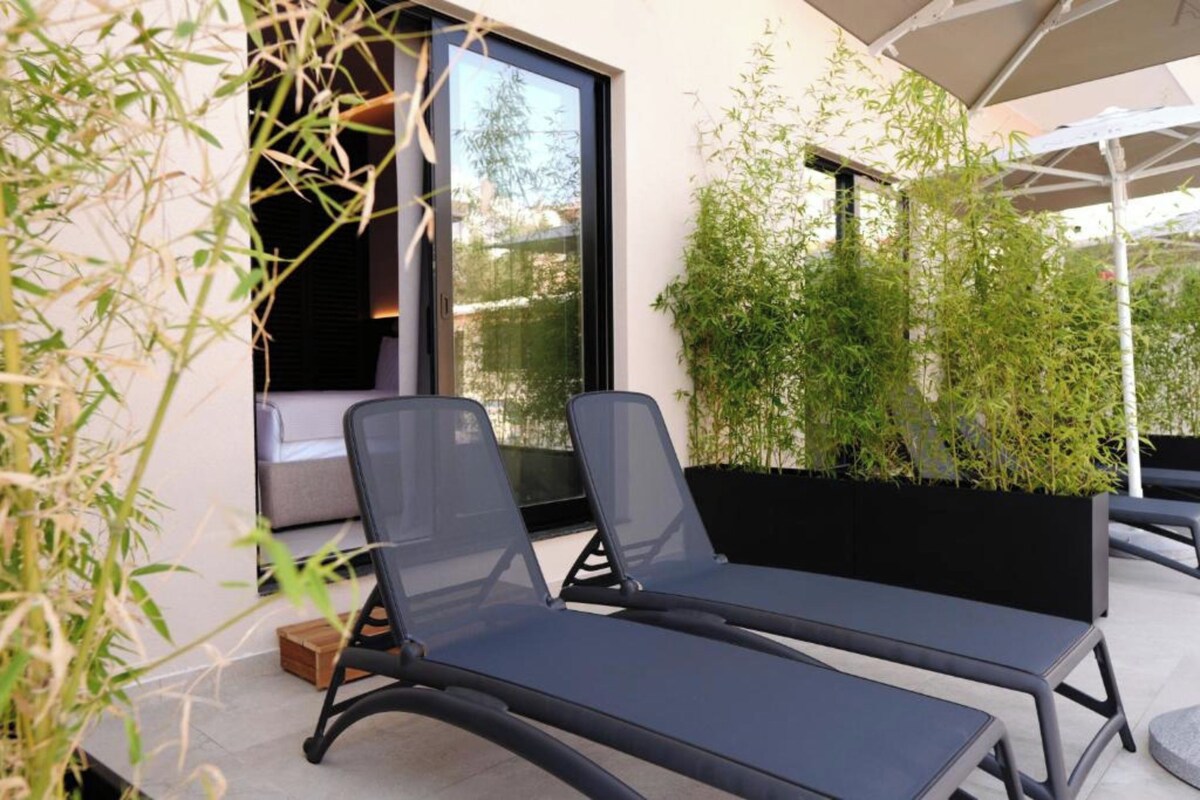 A modern outdoor seating area with two lounge chairs and a large umbrella.