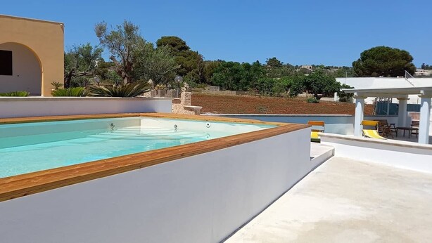 A swimming pool with a wooden deck, a white building with arches, and a view of a hilly landscape. - Apartment 'Appartamento Lucia' with Sea View, Wi-Fi and Air Conditioning (Marina di Pescoluse)