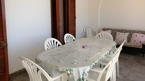 A dining area with a table and chairs, a wooden door, and a sofa with cushions. - Apartment 'Appartamento Lucia' with Sea View, Wi-Fi and Air Conditioning (Marina di Pescoluse)