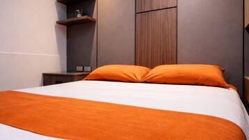 Una habitación de hotel moderna con una cama grande, ropa de cama naranja, una toalla blanca y estanterías de madera empotradas.
