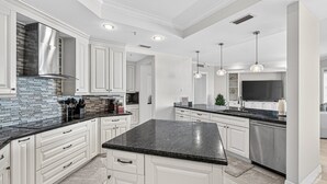 A modern kitchen with white cabinets, a black granite countertop, and stainless steel appliances. - Ultra-Luxury Jupiter Condo!4 En-suite bedrooms! 100 Yards to Ocean! Game Room! (Jupiter)