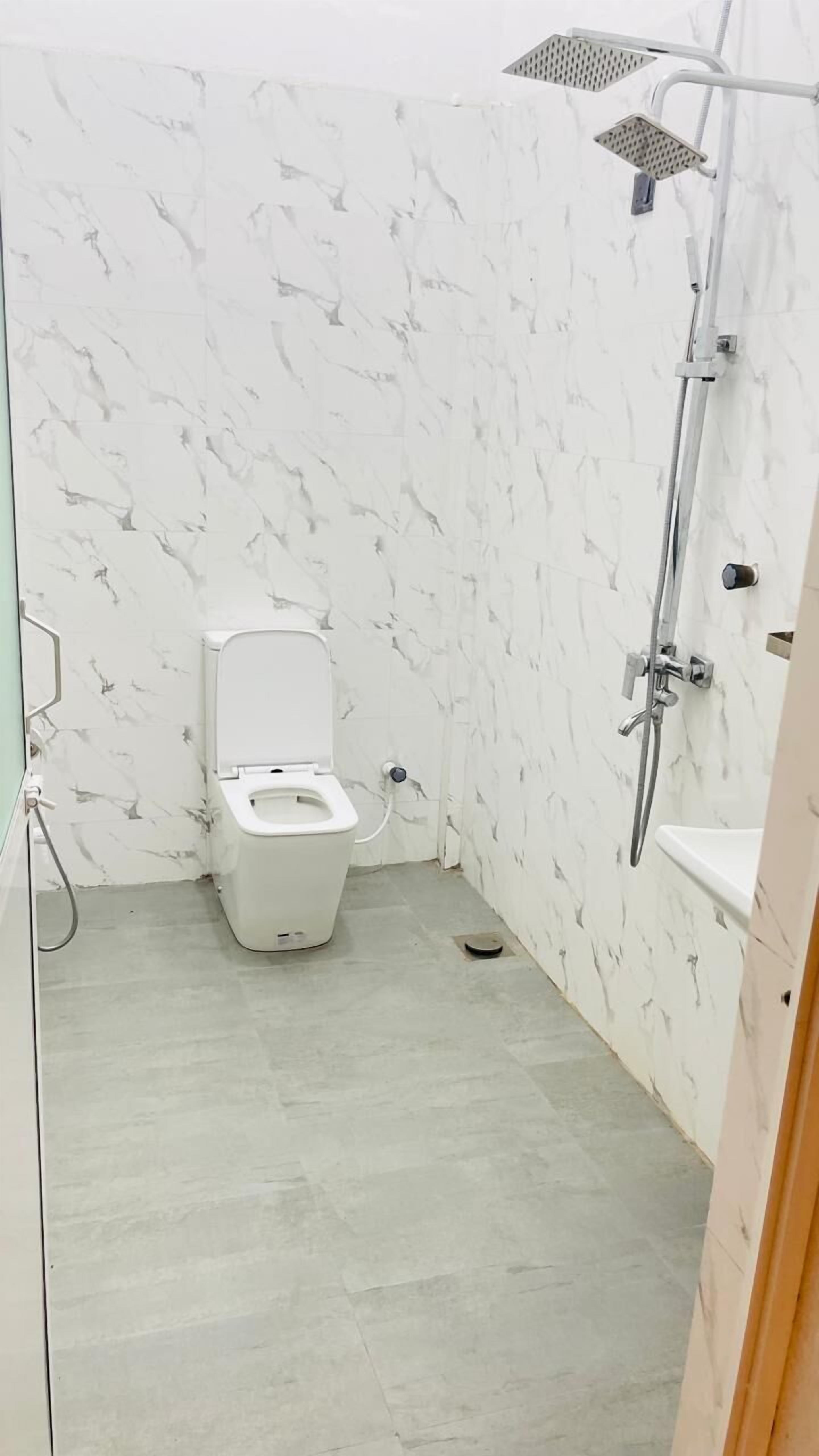 A bathroom with a toilet, a shower, and marble-patterned walls.