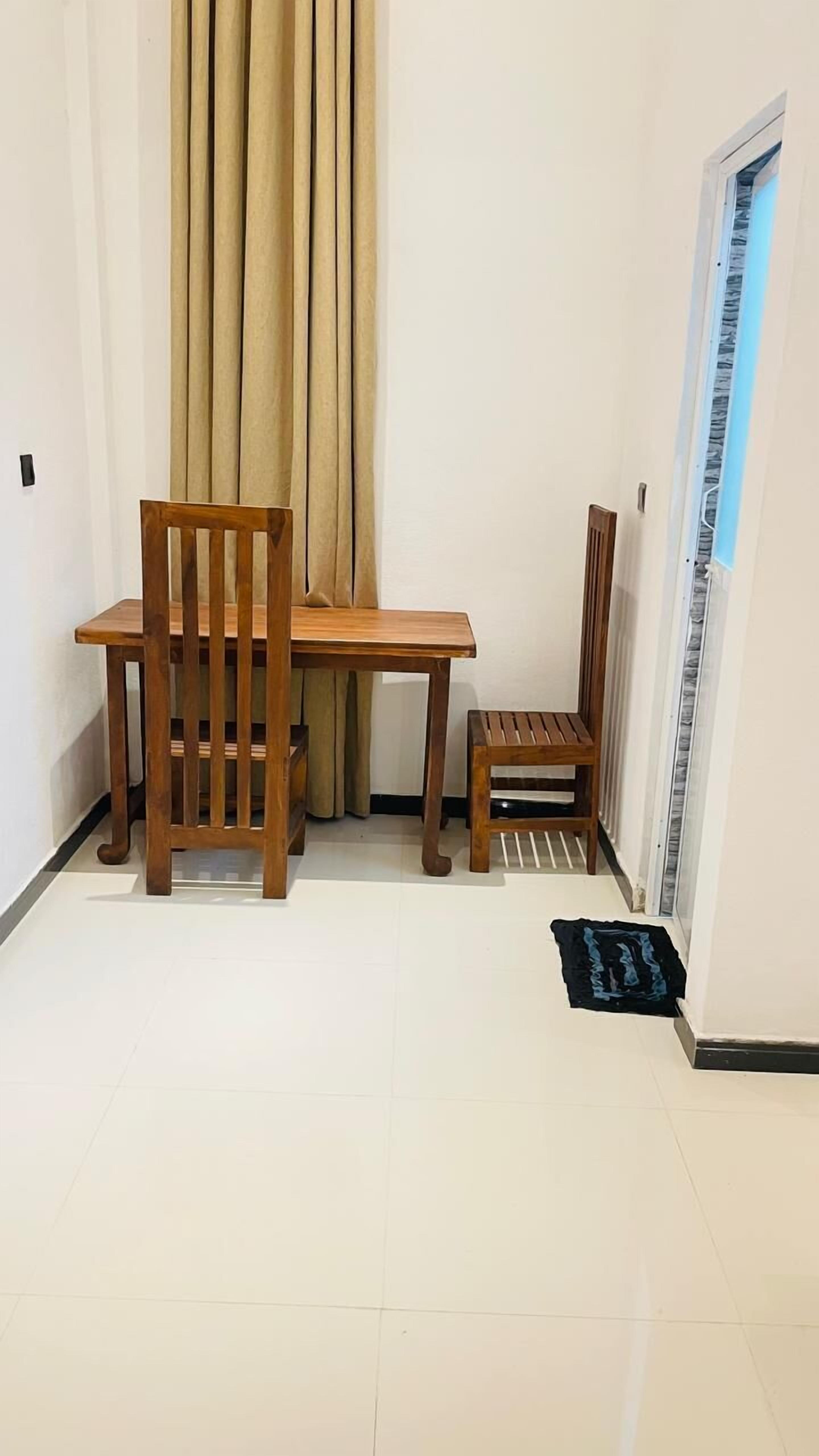 Een kamer met een houten tafel en stoelen, een raam met zonwering en een betegelde vloer.