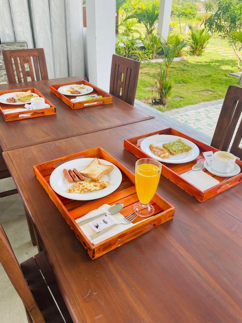 A wooden dining table with trays containing breakfast items like toast, sausage, and a glass of orange juice.
