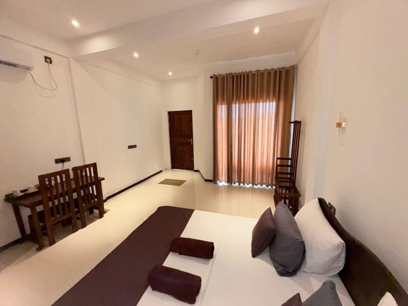 A spacious room with a large bed, a wooden chair, a small table, and a window with curtains.