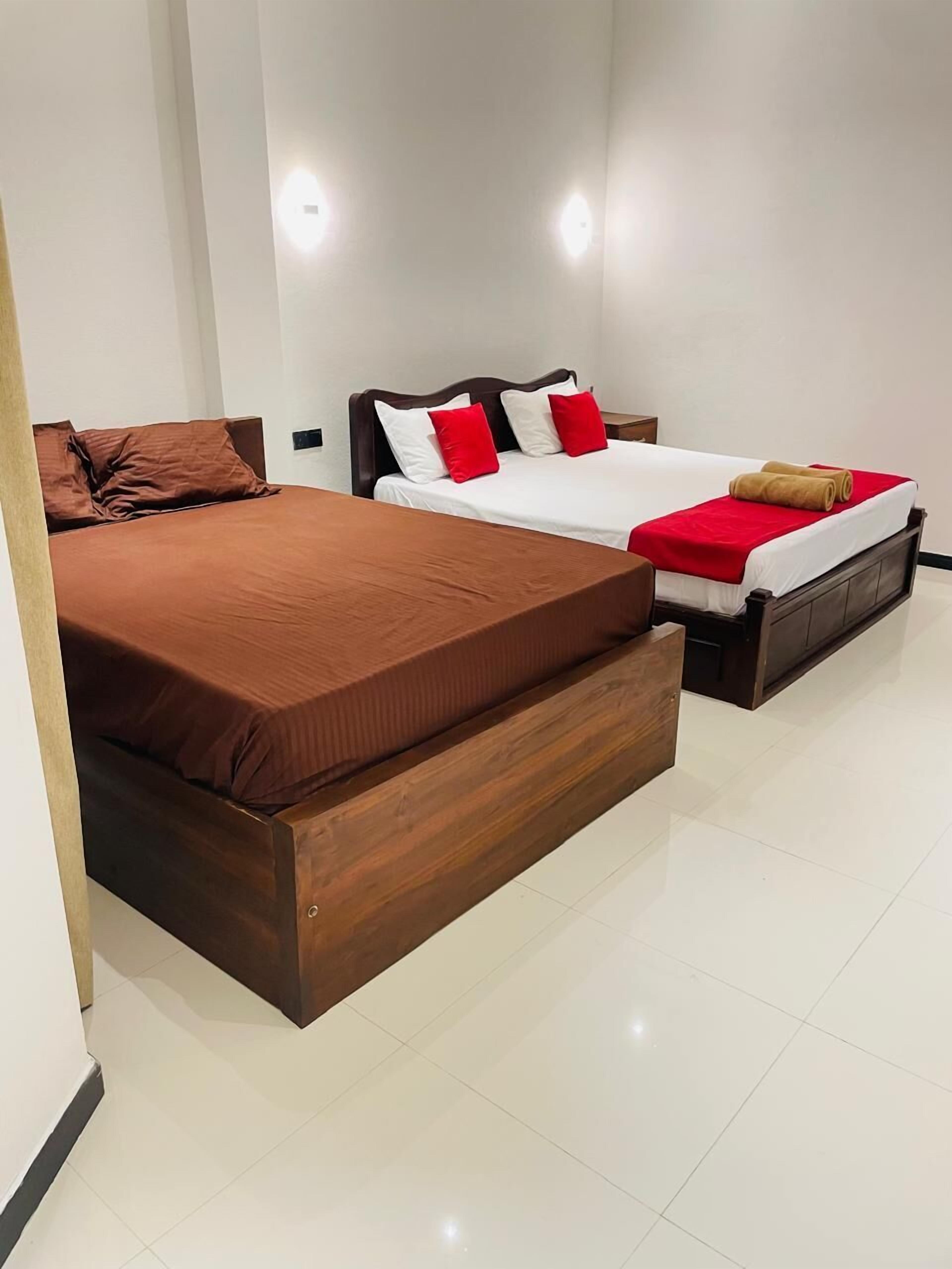 A hotel room with two beds, a wooden bench, and a red and white bedspread.