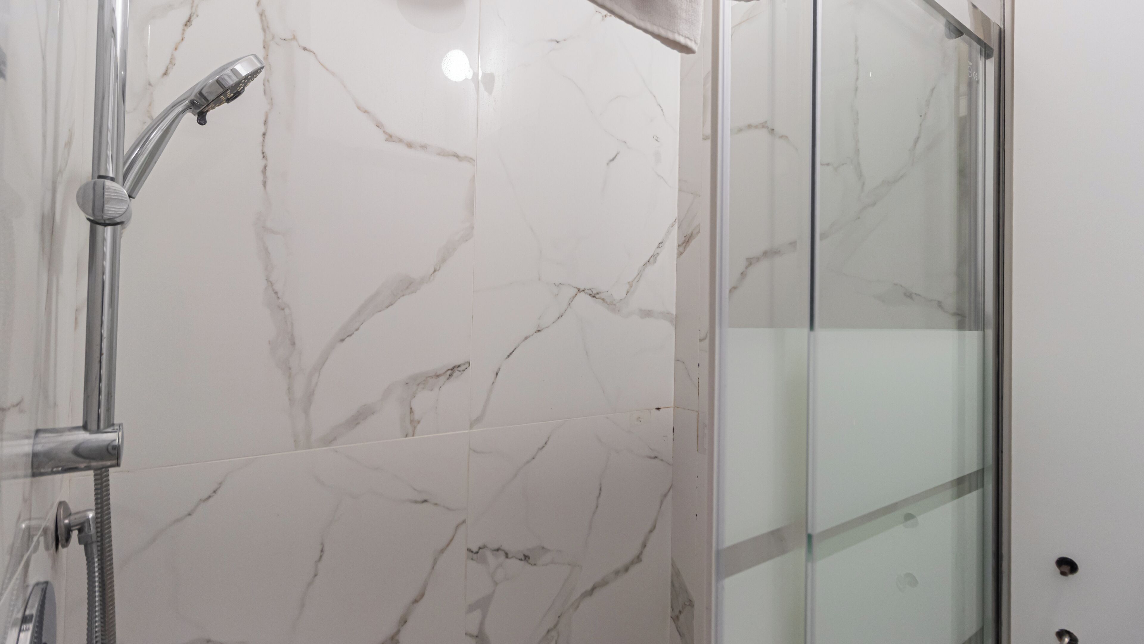 A shower with a glass door and a marble wall.