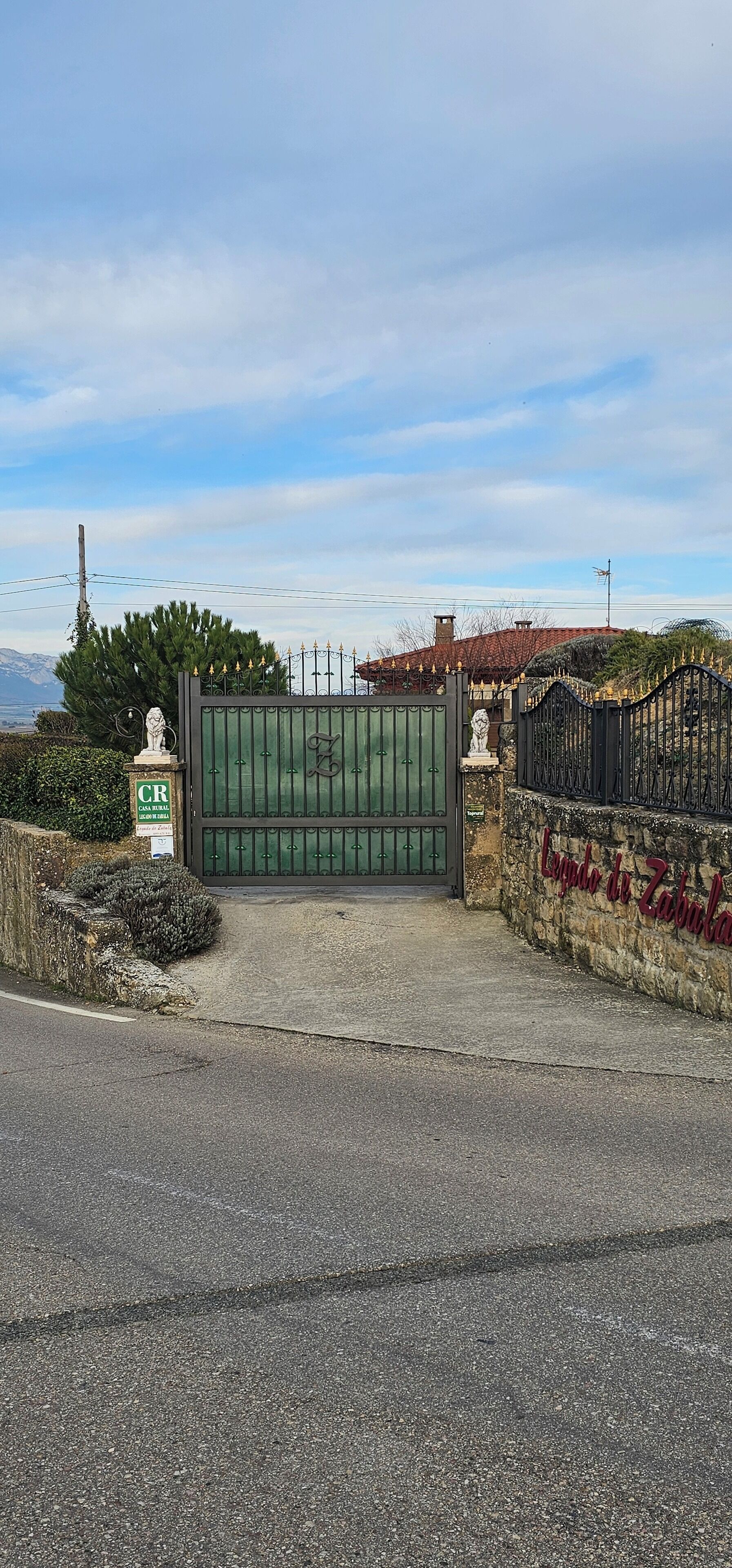 A gated entrance with a green gate, a stone wall with a sign, and a clear sky.