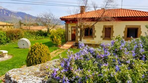 Una casa con tejado rojo, un camino de piedra que lleva a la entrada y un jardín con flores moradas y una escultura de piedra.