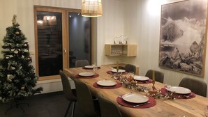 En matplats med ett träbord dukat för fyra personer, omgivet av stolar. Ett julgran syns till vänster.