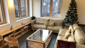 Ett mysigt vardagsrum med en soffa, ett soffbord i glas, en fåtölj i rotting och en julgran.