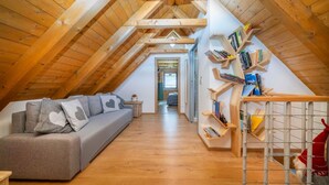 Un dormitorio en el ático con techo de madera, un sofá gris con almohadas con forma de corazón, una estantería y un perro pequeño.