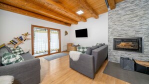 Una sala de estar moderna con pared de piedra, vigas de madera en el techo, un sofá gris y una chimenea.
