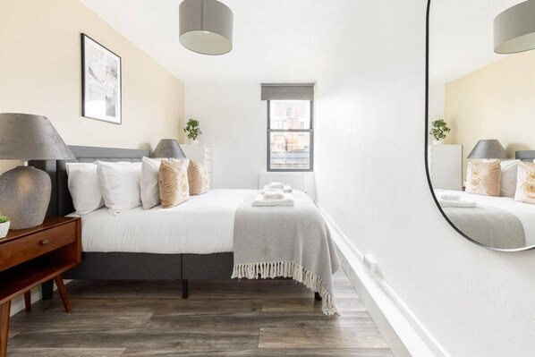 A hotel room with a bed, bedside table, lamp, and a large mirror. - Family/business - Sleeps 3 - Wifi - Near Transport (London)