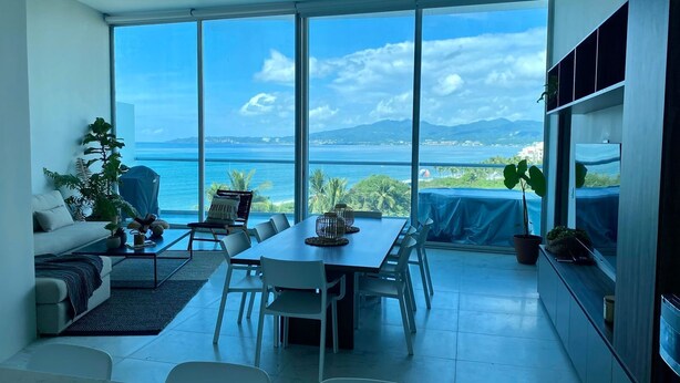 Un soggiorno moderno con un grande tavolo da pranzo, divani bianchi e vista sul mare e sulle montagne.