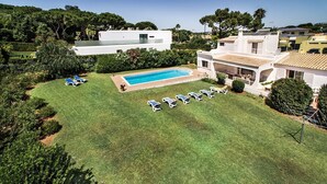Une maison moderne dotée d’une piscine, d’une pelouse avec des chaises longues et d’un jardin.