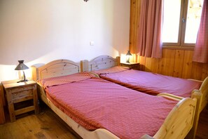 Ein Zimmer mit zwei Holzbettgestellen, jeweils mit einem Kopfteil, einem Nachttisch mit Lampe und einem fenster mit Vorhängen.