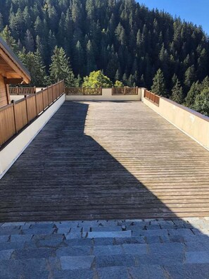 A wooden deck with a stone pathway leading to a building. - Hostcare - Le Paddington - Espace Diamant (Cohennoz)