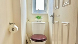 Et lille badeværelse med toilet, toiletpapir, et vindue over toilettet og en dør til højre.
