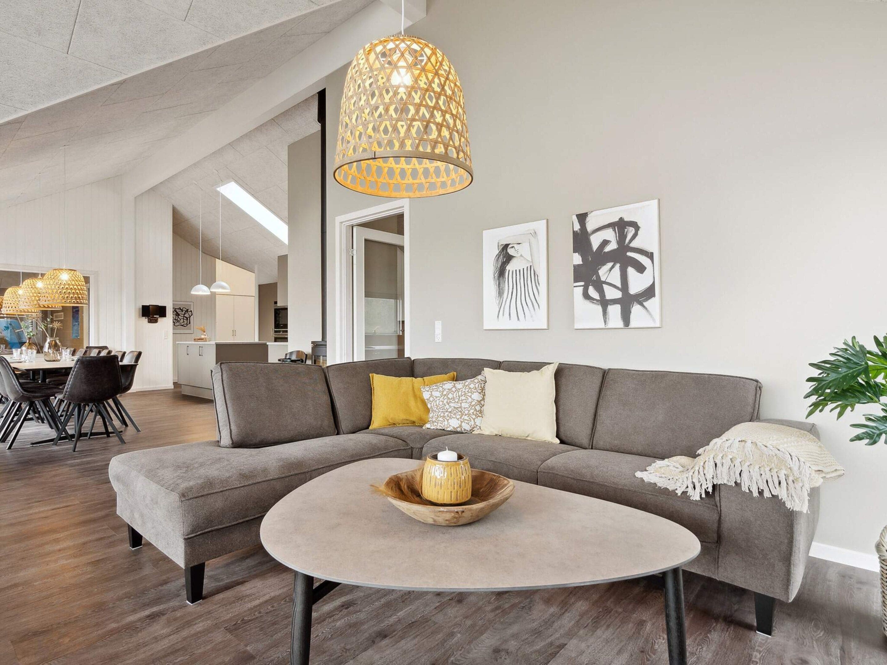 A modern living room with a grey sectional sofa, a round coffee table, and a hanging light fixture.