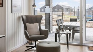 Een moderne woonkamer met een grijze fauteuil, een klein rond tafeltje met kaarsen, en uitzicht op de achtertuin.