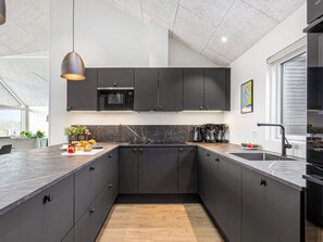 Une cuisine moderne avec des meubles de couleur sombre, un four encastré et un grand îlot central doté d’un évier.