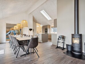 A modern kitchen with a central island, a dining area with a long table and chairs, and a wood-burning stove. - 5 Star Holiday Home in Bogense (Bogense)