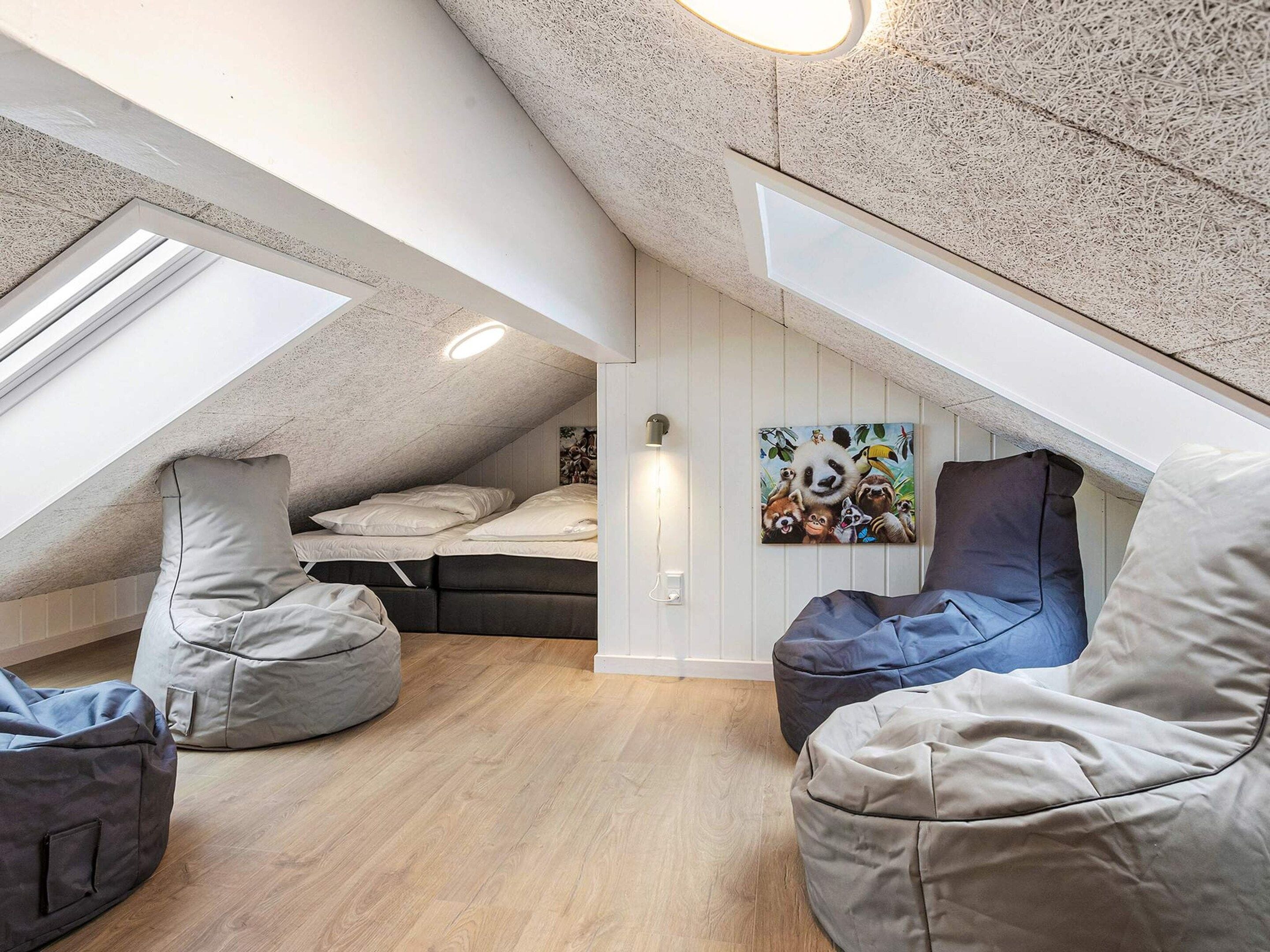 A loft bedroom with a sloped ceiling, skylights, a bed, bean bags, and a wall-mounted light fixture.
