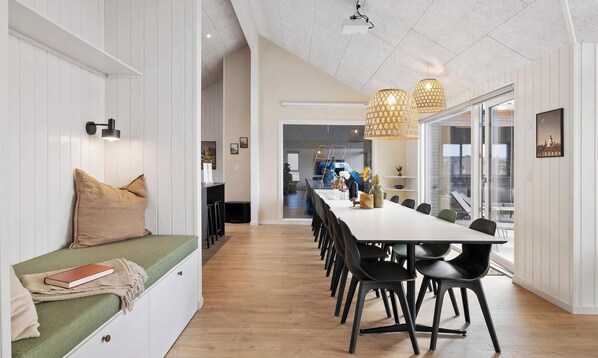 Un espace de salle à manger moderne avec une longue table, des chaises noires et des luminaires suspendus.