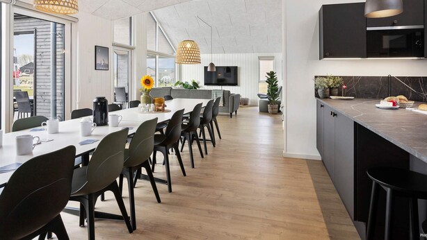Een moderne keuken met een groot schiereiland, een eethoek met een lange tafel, en een woonruimte met een televisie.
