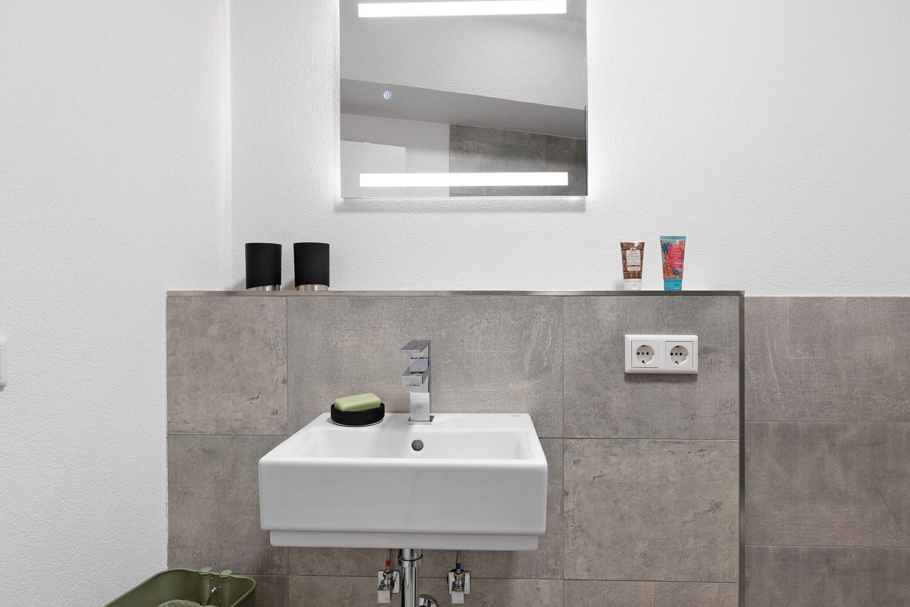 A bathroom with a white sink, a mirror, and a light switch on the wall.