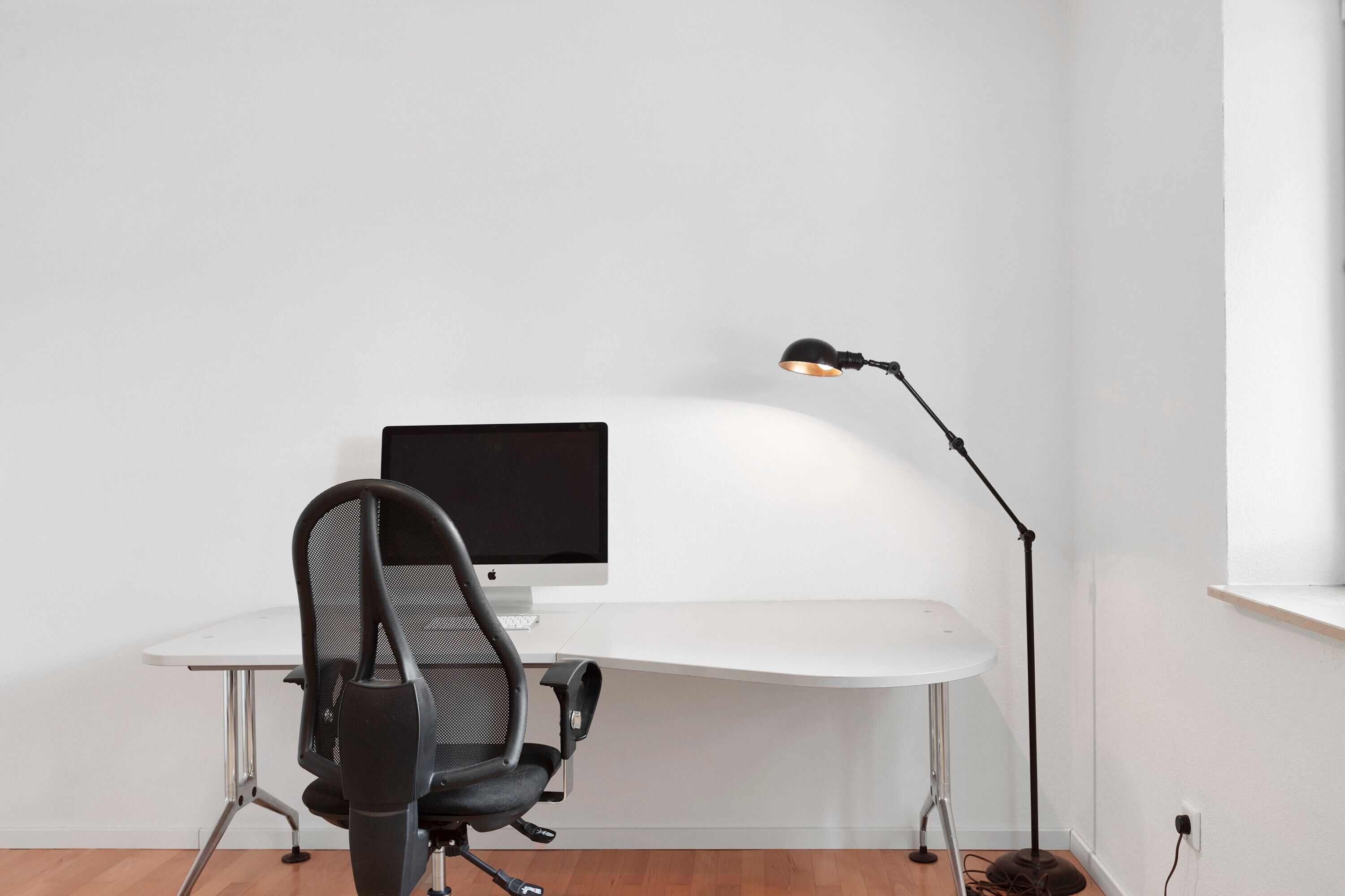 A workspace with a desk, chair, monitor, and desk lamp.