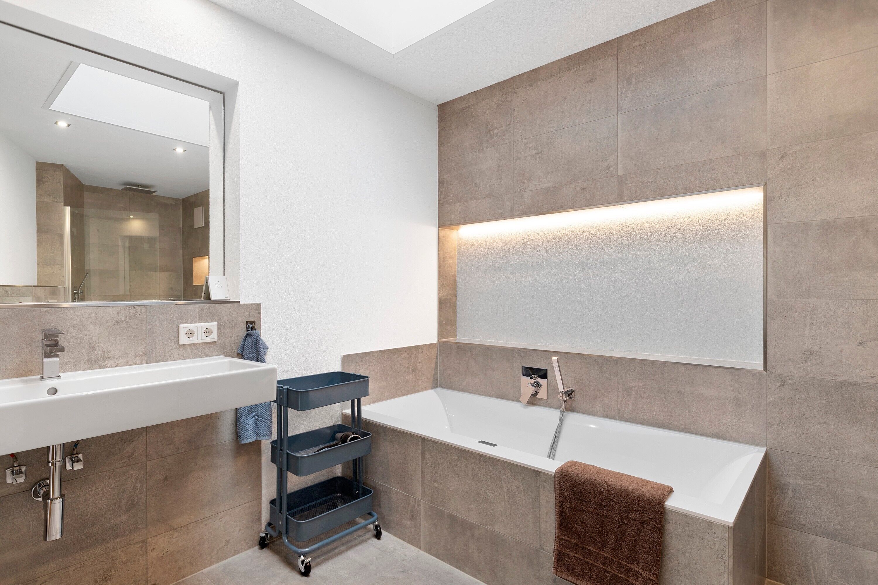 A modern bathroom with a white sink, a bathtub, and a large mirror.