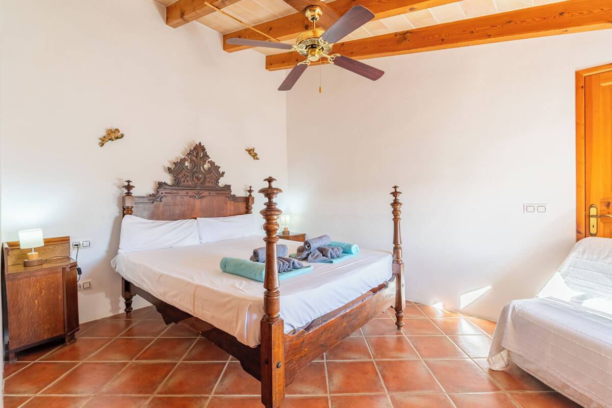Un lit à baldaquin avec une tête de lit en bois, un ventilateur de plafond et une table de chevet avec une lampe.
