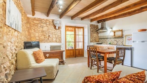 A cozy living room with a sofa, a dining table, and a kitchen area with a refrigerator and stove. - Agroturismo Sa Vall de son Macia (Manacor)