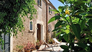 A rustic stone building with a doorway, potted plants, and two wooden chairs. - Agroturismo Sa Vall de son Macia (Manacor)