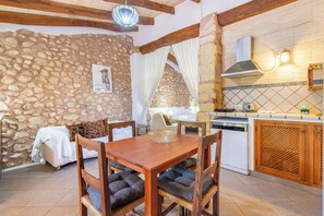 A rustic interior with a stone wall, wooden dining table, and a kitchen area. - Agroturismo Sa Vall de son Macia (Manacor)