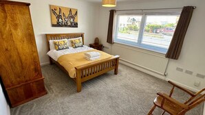 A bedroom with a wooden bed, a window with blinds, a wooden chair, and a painting on the wall. - Detached 3 En-Suites Parking 5 Double Rooms (Colchester)