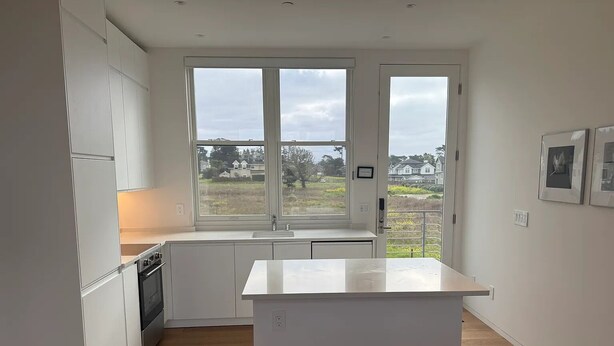 Uma cozinha moderna com armários brancos, uma ilha central e uma grande janela com vista para o exterior.