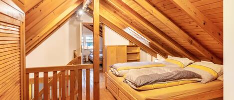 Un dormitorio estilo loft con techo inclinado, una cama con almohadas y barandilla de madera.