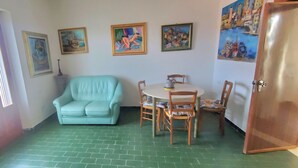Una habitación con suelo de baldosas verdes, un sofá azul claro, una mesa redonda con sillas y cuatro cuadros enmarcados en la pared.