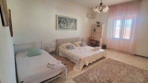 Un dormitorio con dos camas, un escritorio, una silla, un tapete estampado y un cuadro en la pared.