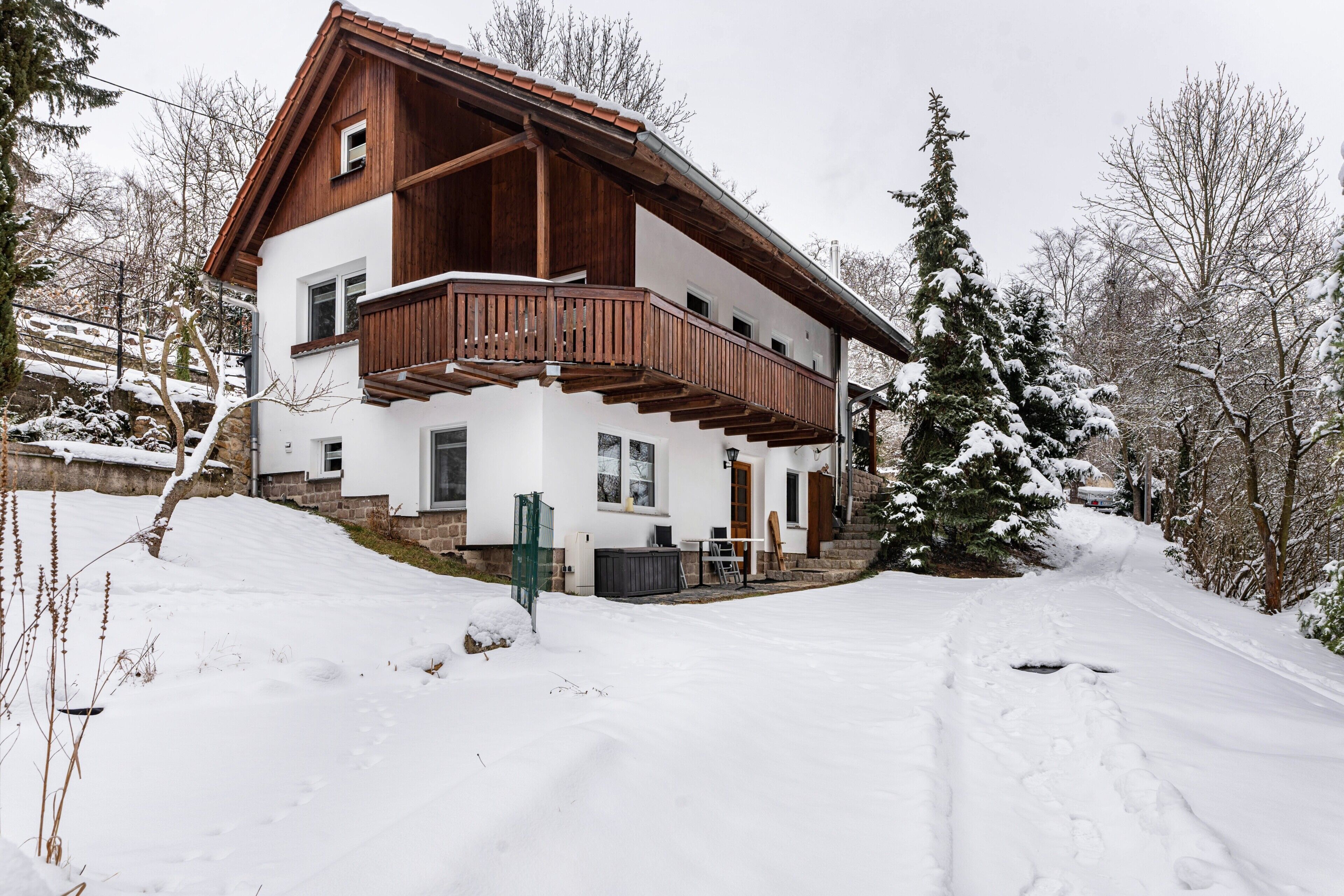 Una casa a due piani con un balcone in legno, una scala in pietra e un vialetto coperto di neve.